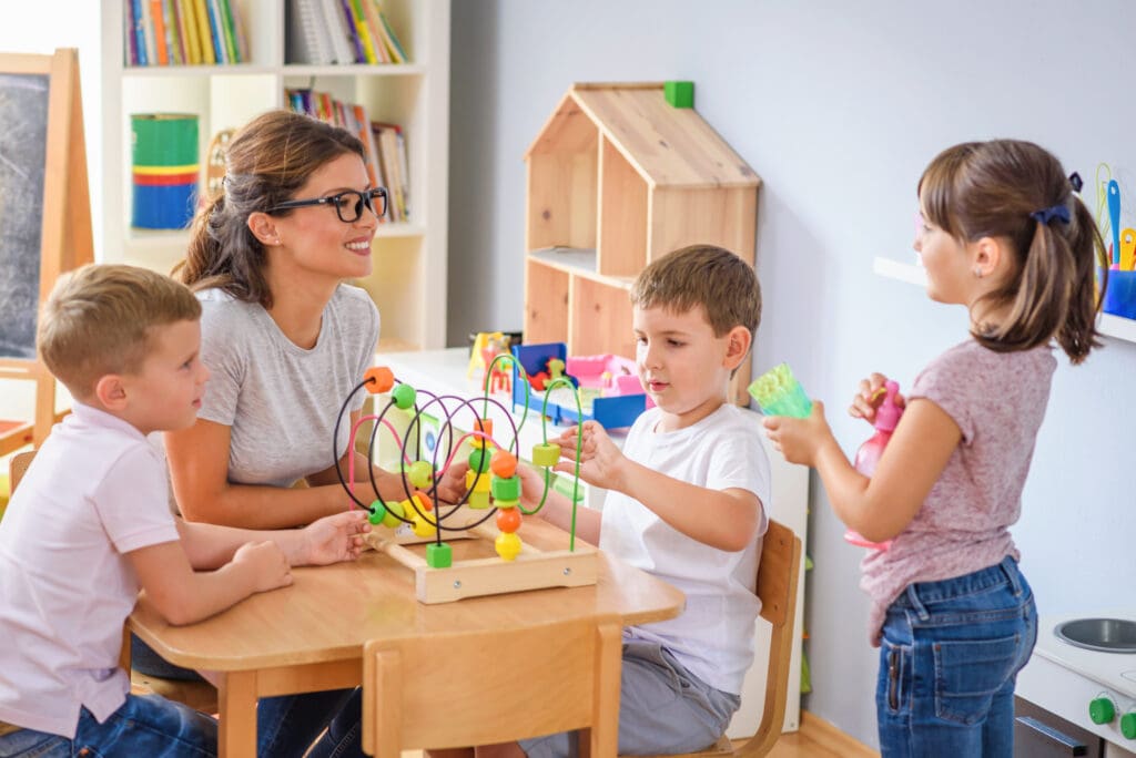 Preschool teacher with children playing with colorful wooden didactic toys at kindergarten