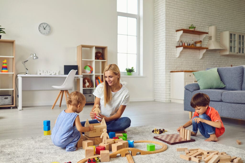 Happy mother and her two children at home, playing with lots of wood blocks, building big toy city
